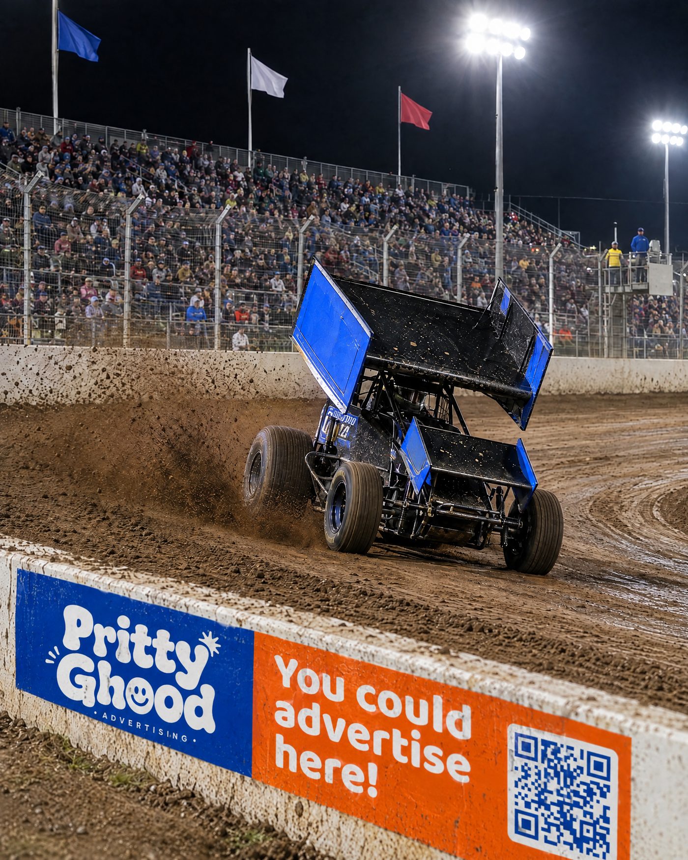 A sprint car sliding past a Pritty Ghood banner on the track wall in front of a packed grandstand at night