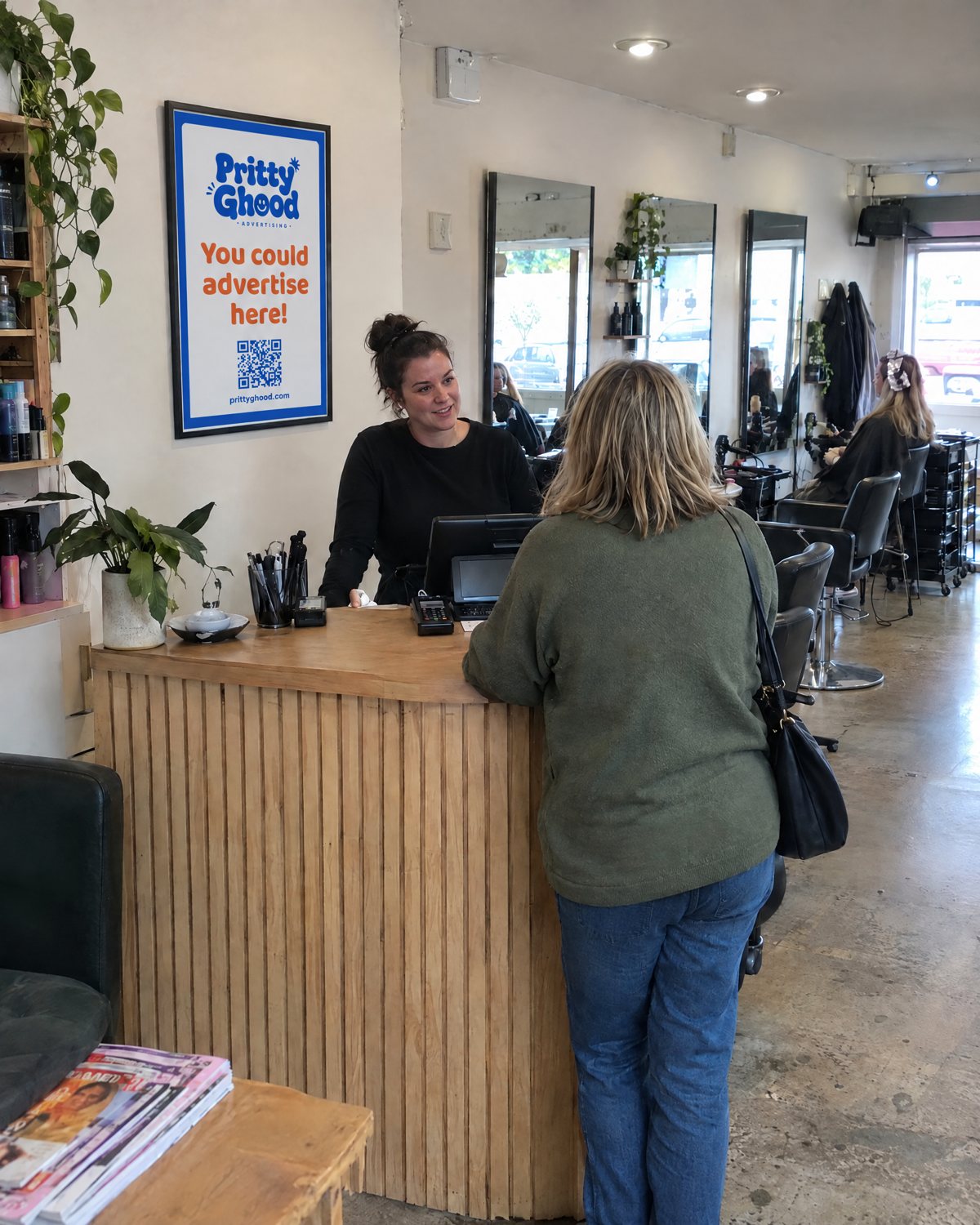 A salon reception desk with a framed Pritty Ghood poster on the wall behind it